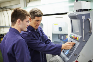 Engineer And Apprentice Using Automated Milling Machine